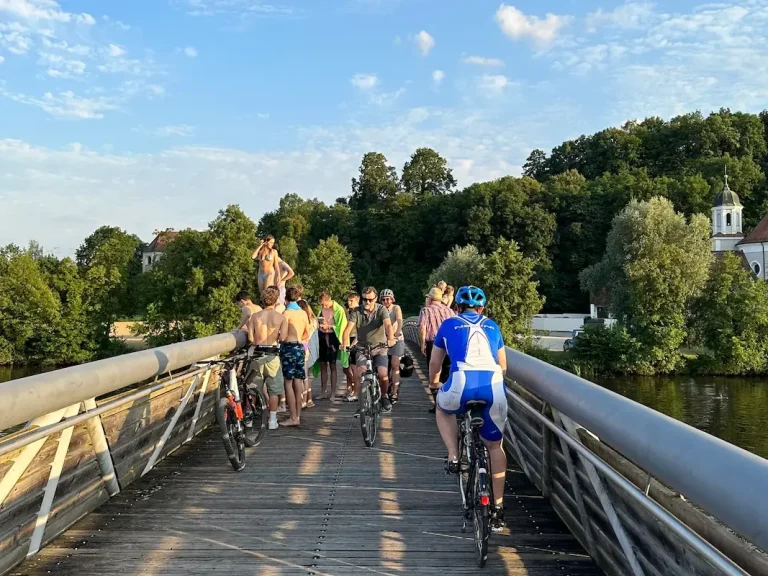 Freizeitspaß pur: Radfahren und Baden direkt vor der Haustür des Hotel Krieger. Radfahrer auf der Brücke und Badegäste beim Sprung in die Naab – Sommeridylle direkt am Hotel Krieger in Mariaort bei Regensburg.
